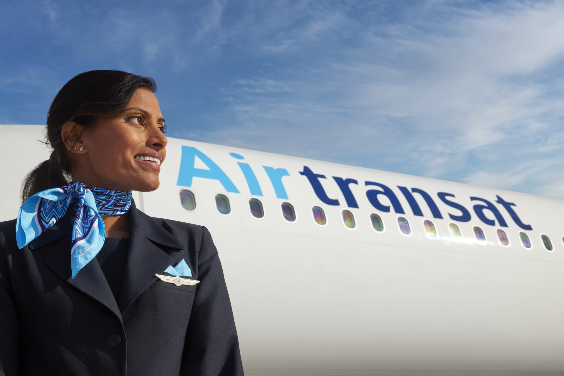 A Transat flight attendant standing in front of a plane.